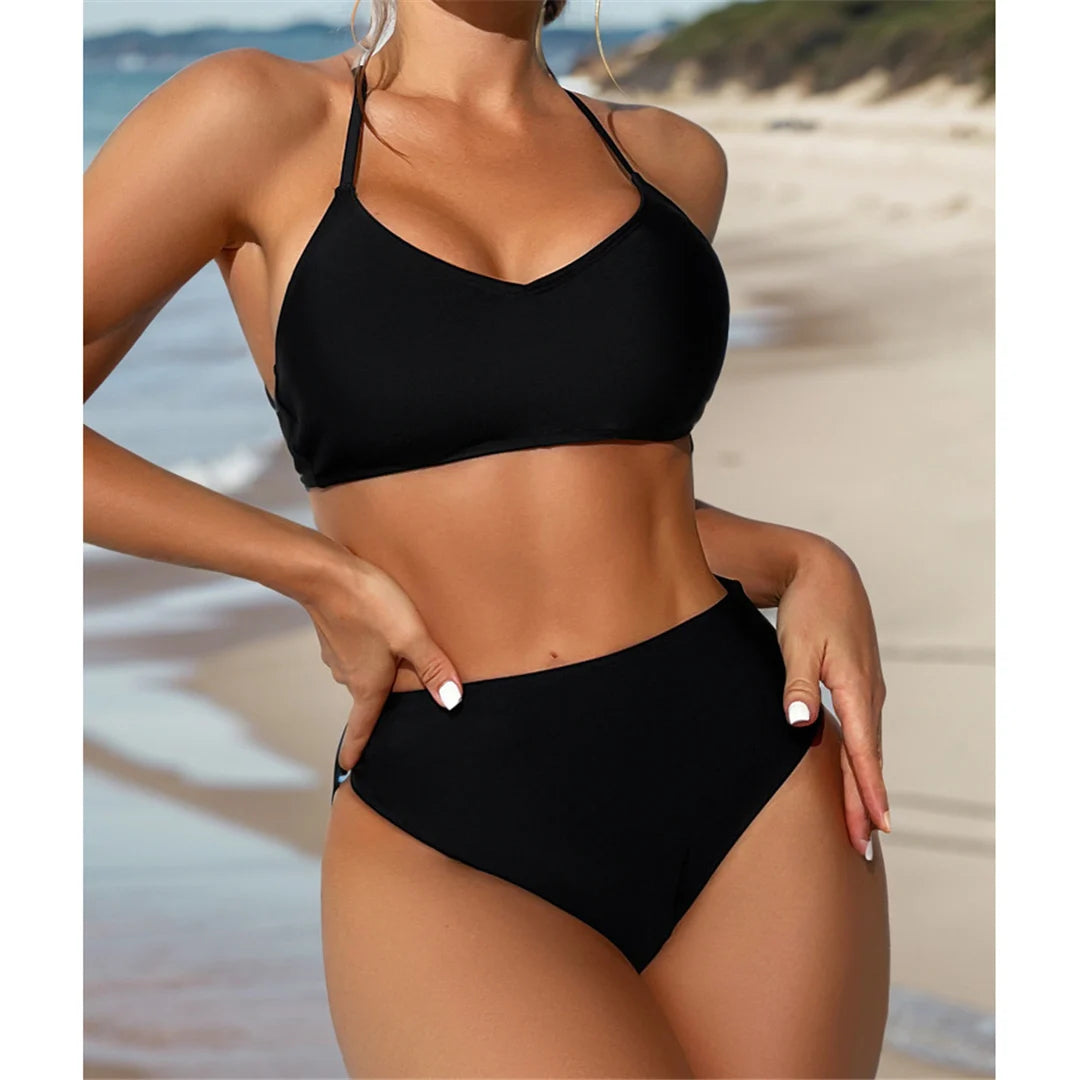 Women's high waisted bikini set in solid black, featuring a cheeky cross back design and wire-free support, crafted from nylon and spandex for a comfortable and flattering fit, ideal for beach days.