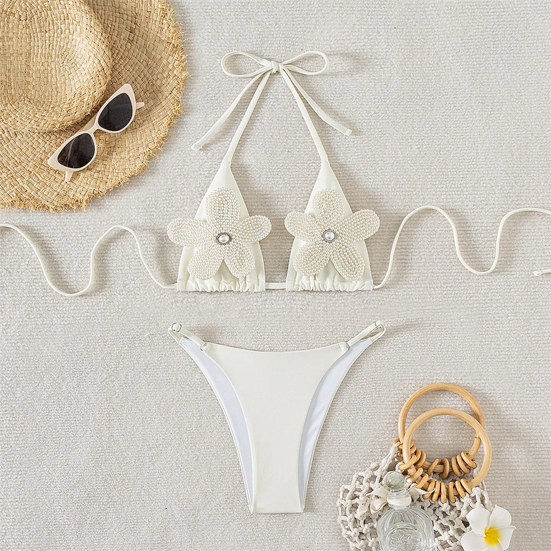 Delicate two-piece bikini set in white for women, adorned with 3D flowers and pearls. Features a flattering high-leg cut design made from Nylon and Spandex. Low waist design with wire free support. This floral pattern bikini fits true to size and includes a pad. Available in sizes XS, S, M, and L. Offers free shipping for this exquisite choice for sun-drenched occasions. Ideal for women aged 18 to 35.