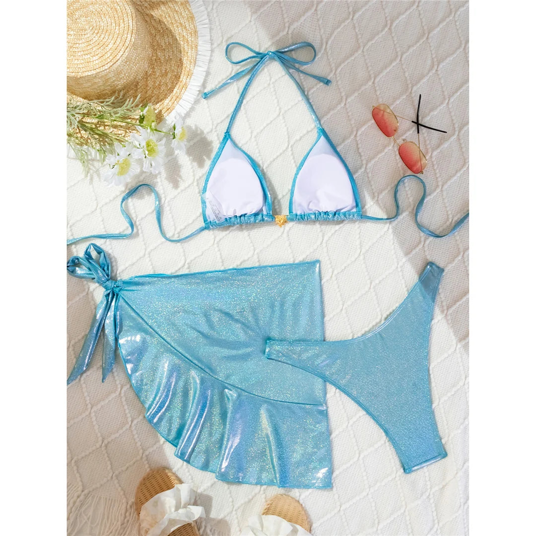 Shiny halter Brazilian bikini three-piece set in solid blue, featuring a shimmering finish and matching sarong, made from polyester and spandex.